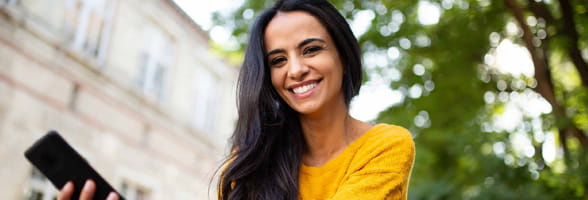 young woman smiling with mobile phone in hand outside