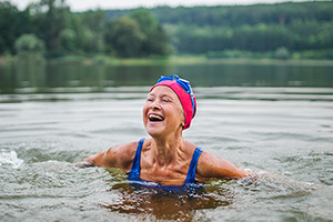 Woman in swimsuit and swimming hat enjoying a cold water swim in a lake on a brisk day.